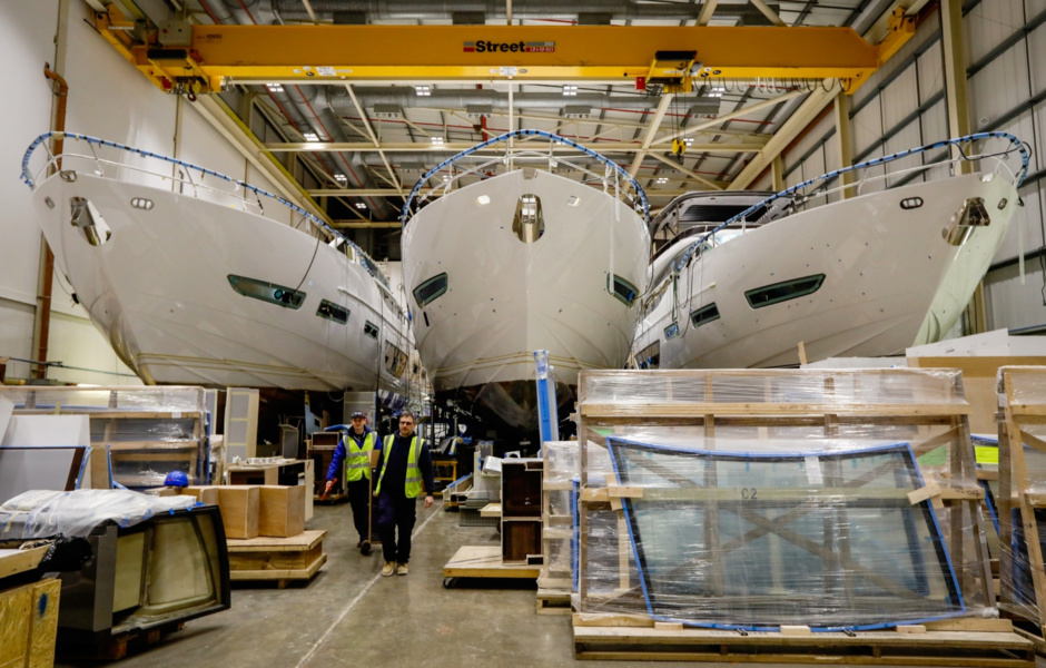 Workers walk past three 85-foot yachts under construction.